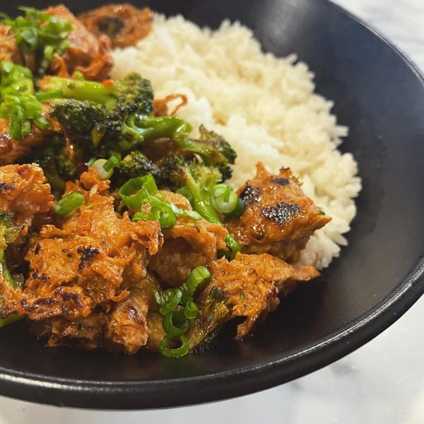 Lazi Cow's Asian dish with orange chicken, broccoli, and white rice, garnished with green onions.