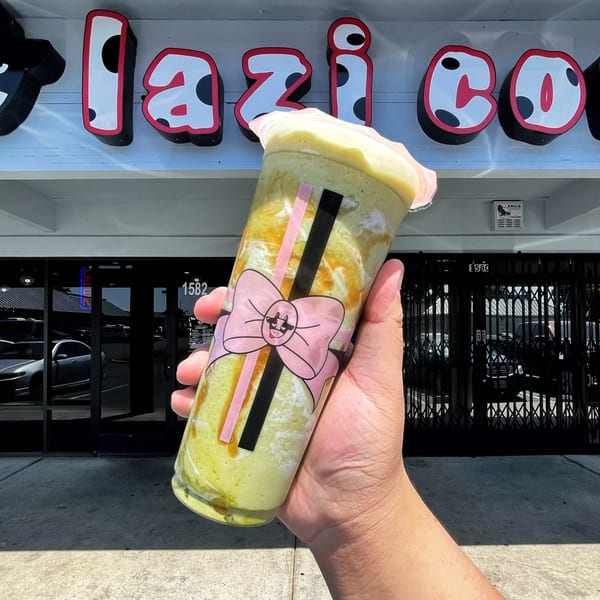 Hand holding a Lazi Cow matcha drink with a pink bow design in front of the store.
