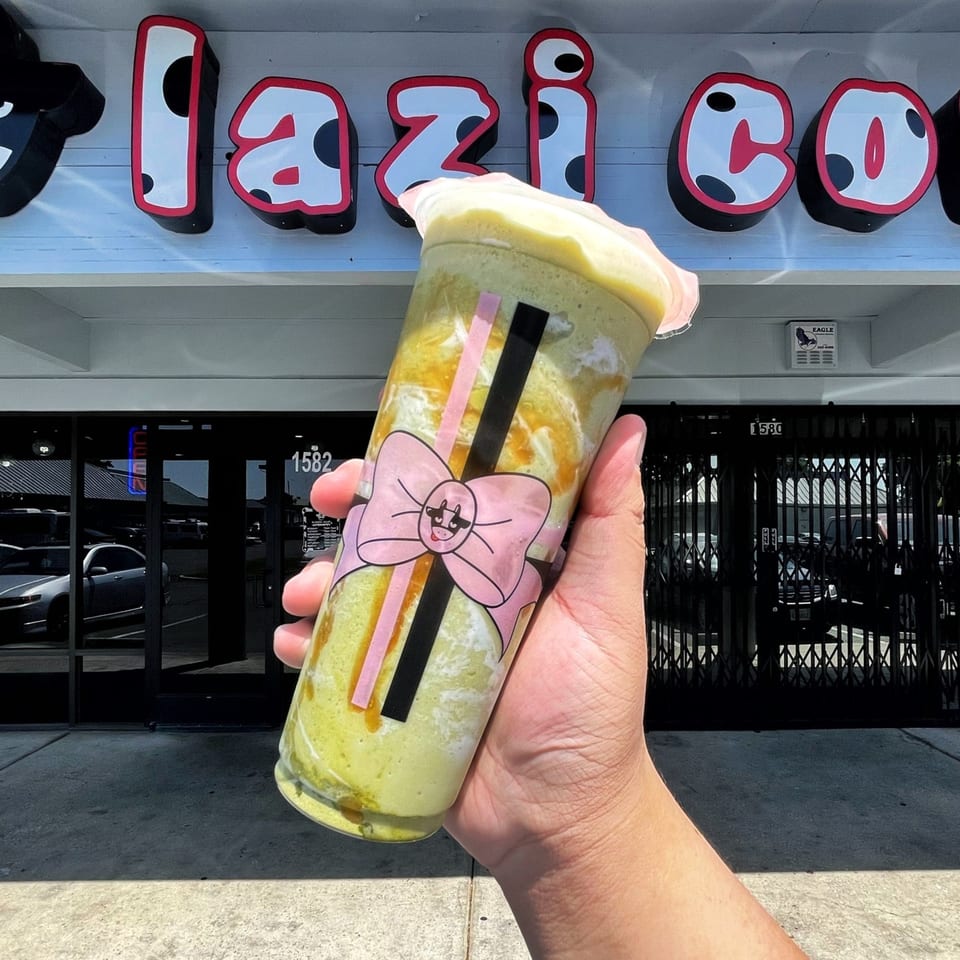 Hand holding a Lazi Cow matcha drink with a pink bow design in front of the store.