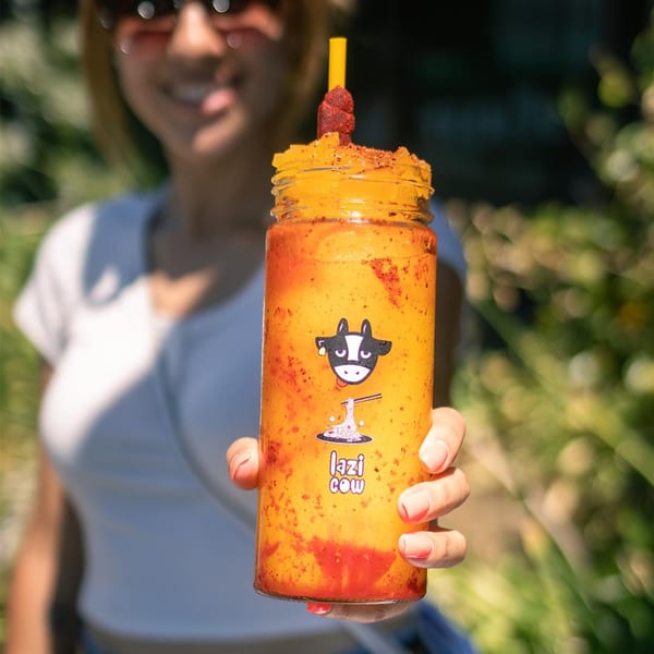 A person holds a Lazi Cow mango drink with chili powder and a tamarind candy straw.