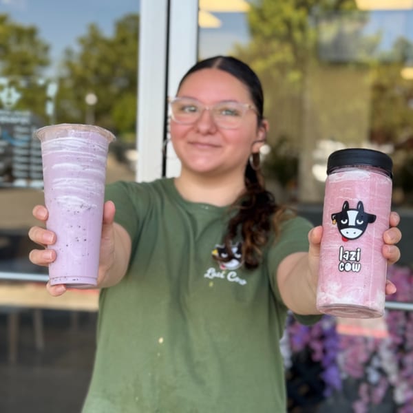 A Lazi Cow employee holds out two colorful Lazi Cow drinks, one purple and one pink.