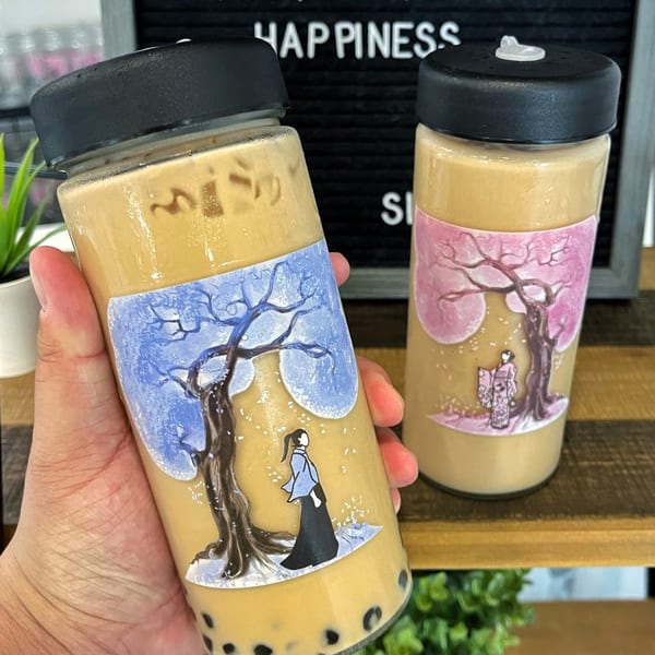 Hand holding a Lazi Cow boba tea with a winter-themed label, another on a shelf.
